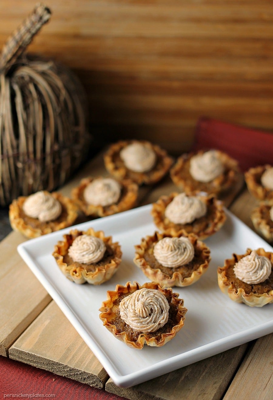 Mini Sweet Potato Pies with Cinnamon Cream Cheese Frosting are super easy to make but look fancy. Impress your guests with these bite sized treats! | www.persnicketyplates.com #pie #sweetpotatopie #thanksgiving #minidessert #dessert white plate of mini sweet potato pies topped with cream cheese frosting