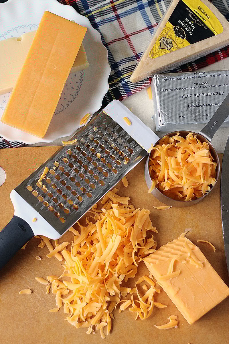 Homemade Baked Macaroni and Cheese is a delicious, super rich, five cheese baked mac and cheese recipe. This copycat steakhouse recipe is fancy enough to serve to guests for holidays, but so delicious, you'll want to make this easy baked mac and cheese recipe every day! grater and cheese on cutting board for homemade baked mac and cheese