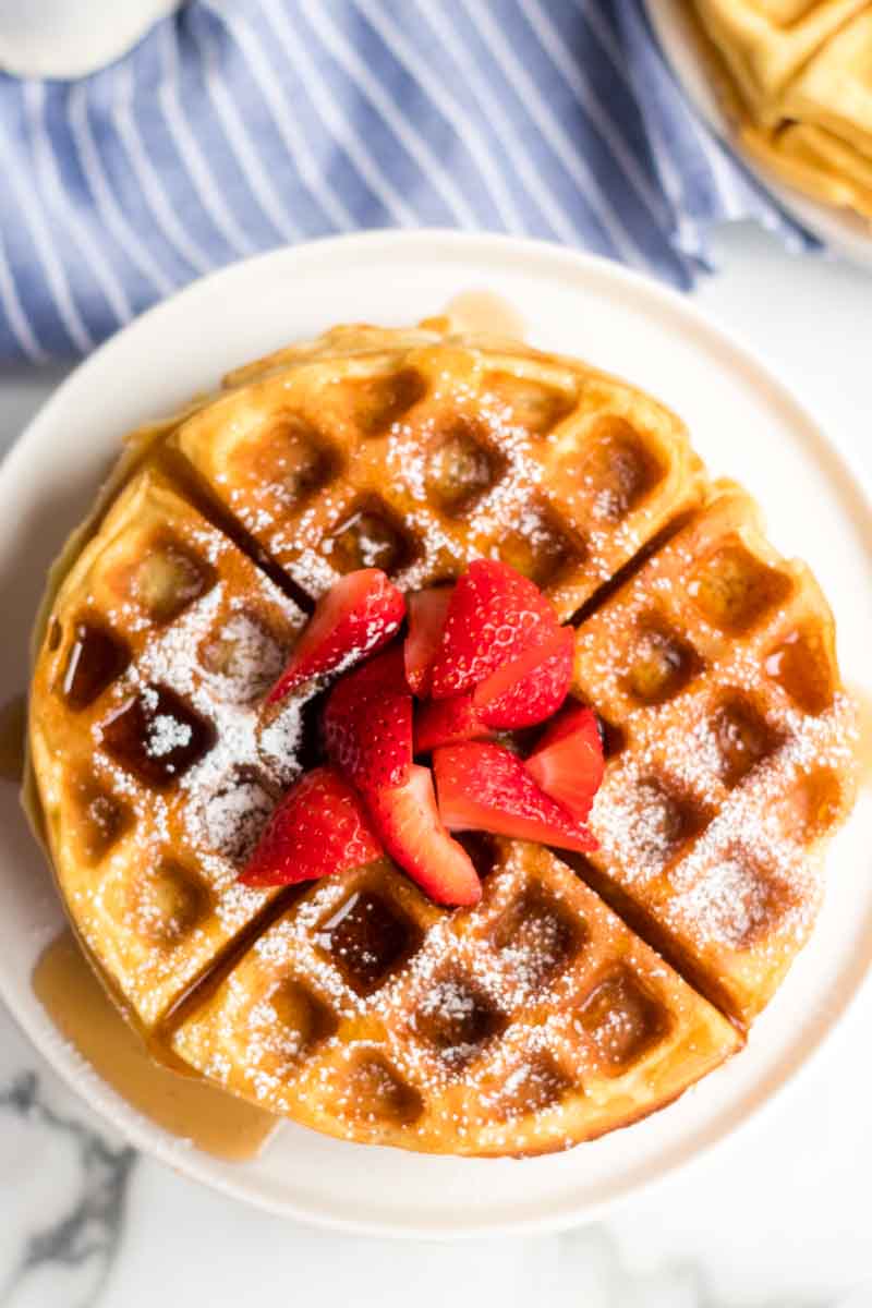 stack of waffles with syrup, powdered sugar, and strawberries