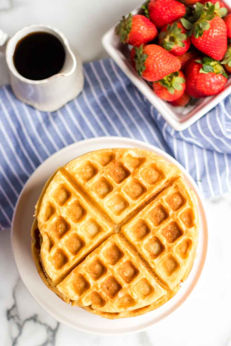 stack of buttermilk waffles with syrup cup and strawberries