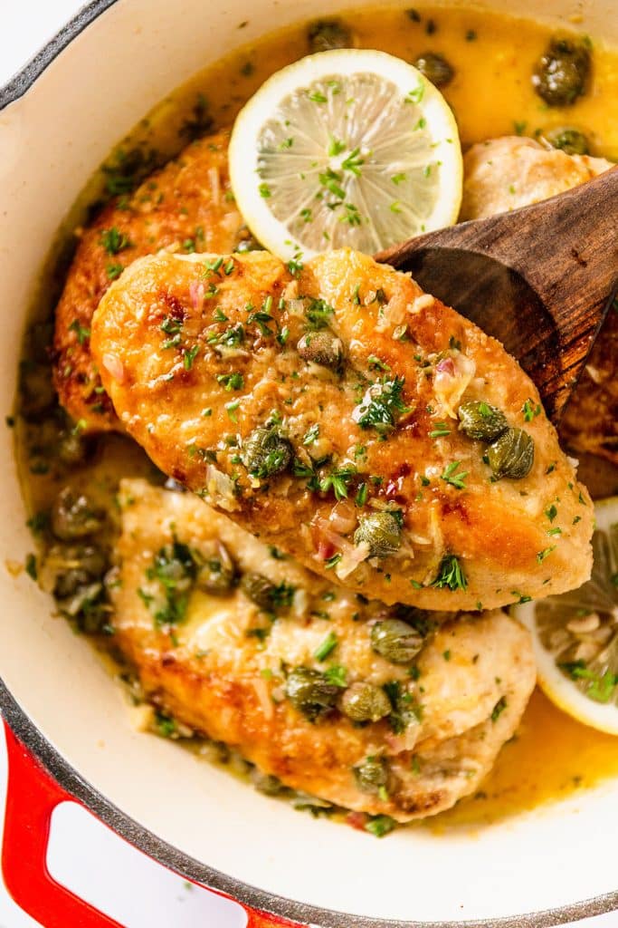 a wooden spoon lifting a chicken piccata breast from a pot.
