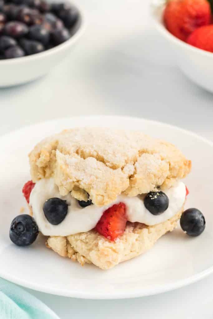 mixed berry shortcake on a white plate next to bowls of berries.