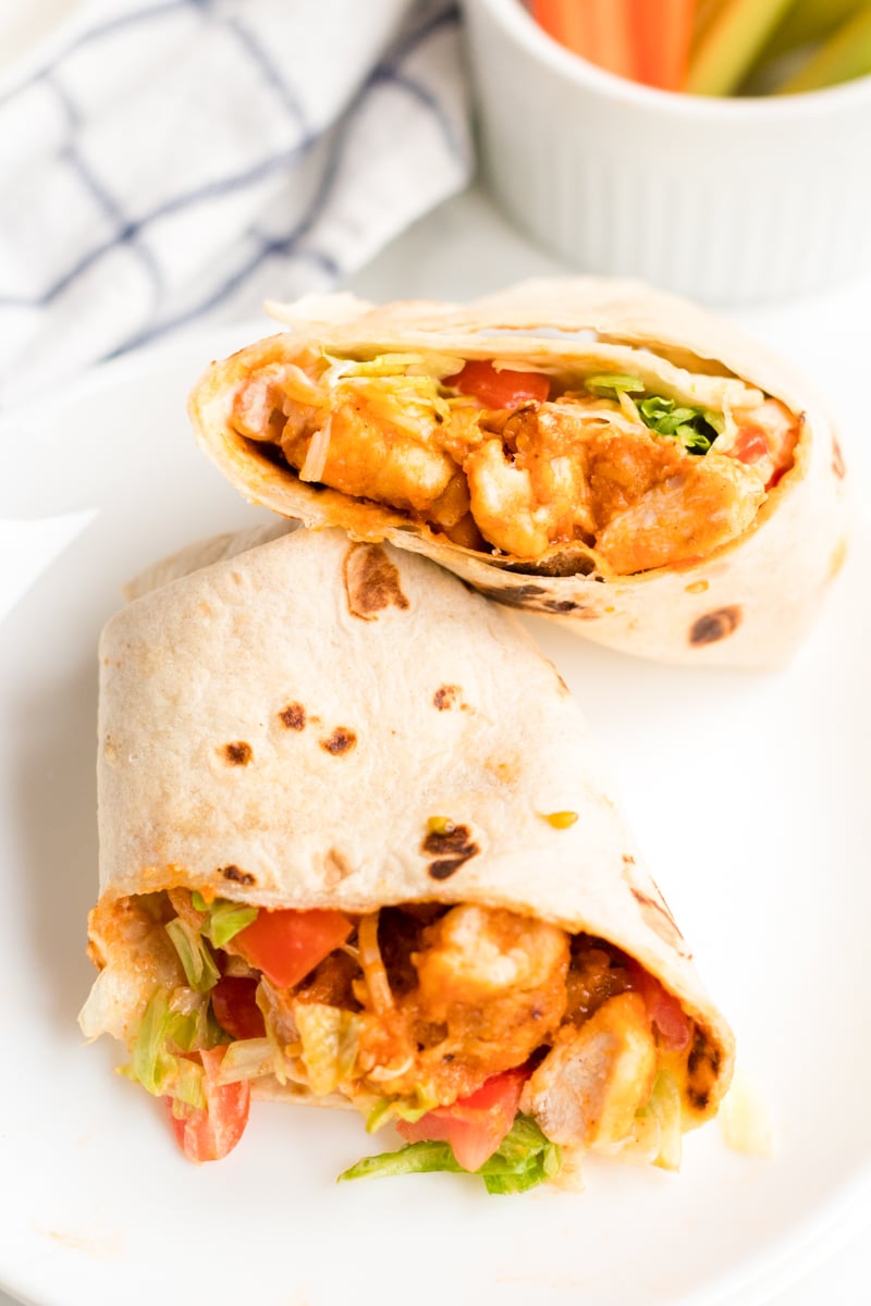If you like the Buffalo Ranch Chicken Wrap from Buffalo Wild Wings, you'll love this lightened up homemade version! Lightly breaded buffalo chicken pieces wrapped up in a soft tortilla with ranch dressing, shredded lettuce, cheese, and tomatoes make a great dinner or the perfect game day meal! | www.persnicketyplates.com sliced buffalo ranch chicken wrap on a white plate