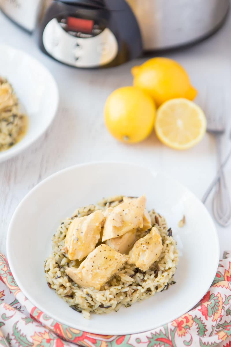 This Crock Pot Lemon Chicken is so easy and perfect for a busy weeknight. This 4 ingredient, quick chicken dinner is amazingly flavorful and sure to be your new favorite meal. Serve with vegetables and ready to serve rice for a fast healthy dinner! | www.persnicketyplates.com lemon chicken on wild rice with slow cooker & lemons in background