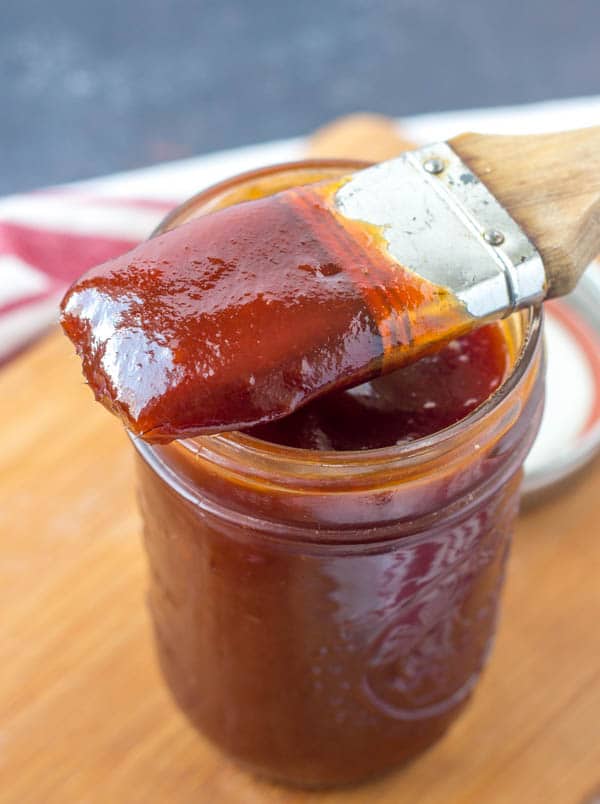 basting brush sitting on top of a mason jar of bbq sauce.