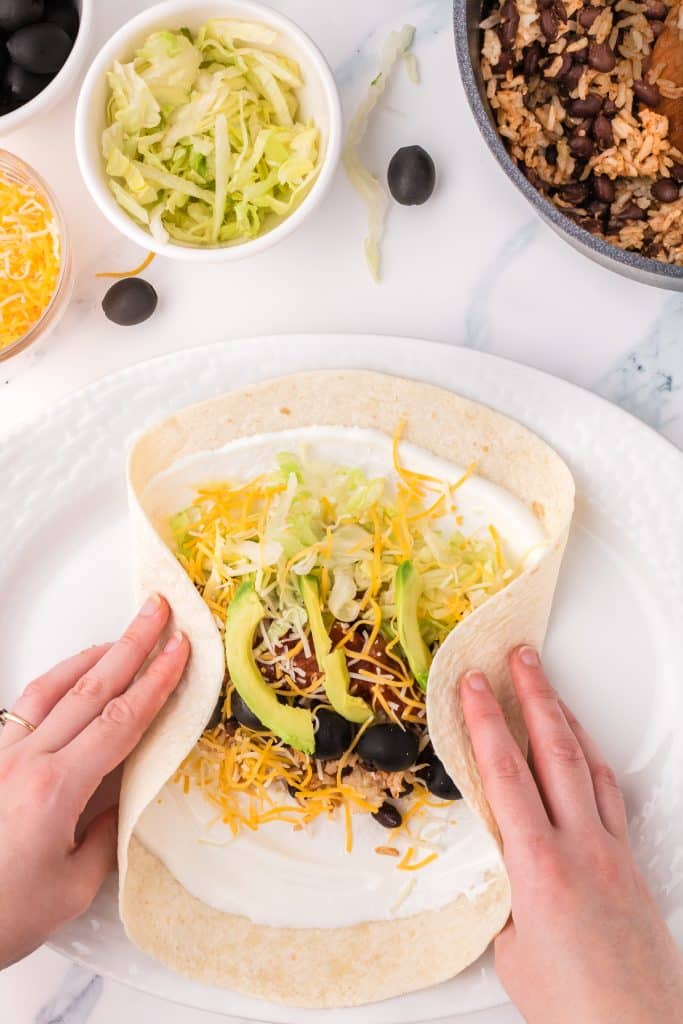 hand wrapping up a tortilla filled with rice, beans, and veggies.