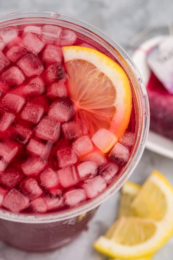 Overhead view of a lemon wedge in a cup of pink iced tea with lots of ice.