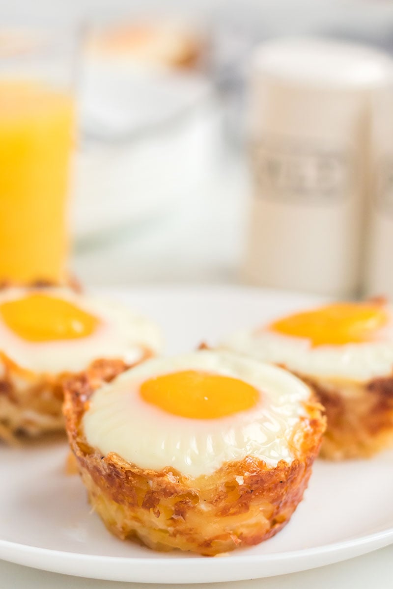 Bird's Nest Breakfast Cups are a fun way to eat eggs and hash browns for breakfast. These baked egg cups combine hash browns and cheese to form a "nest" and are topped with an egg. | www.persnicketyplates.com three hash brown egg cups on a white plate