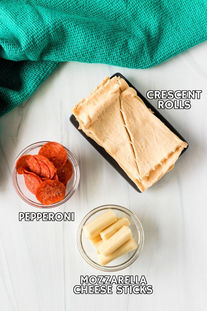 overhead shot of crescent roll dough, pepperoni, and cheese sticks laid out in prep bowls.