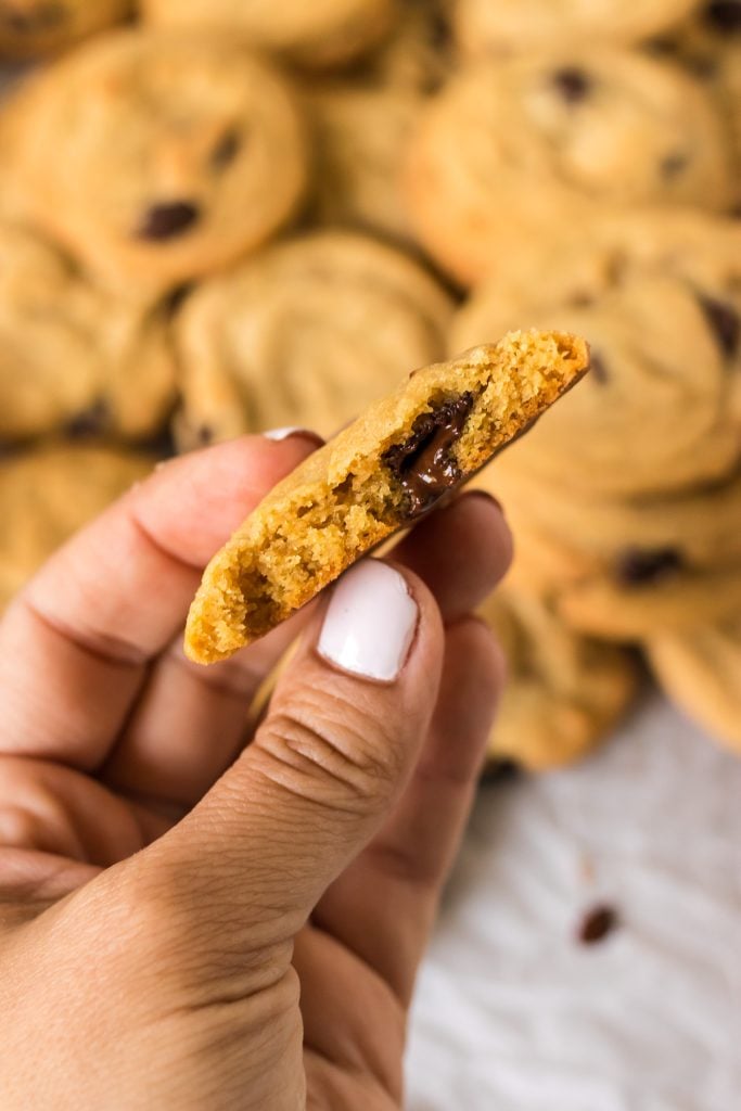 hand holding a chocolate chip cookie with a bite missing.