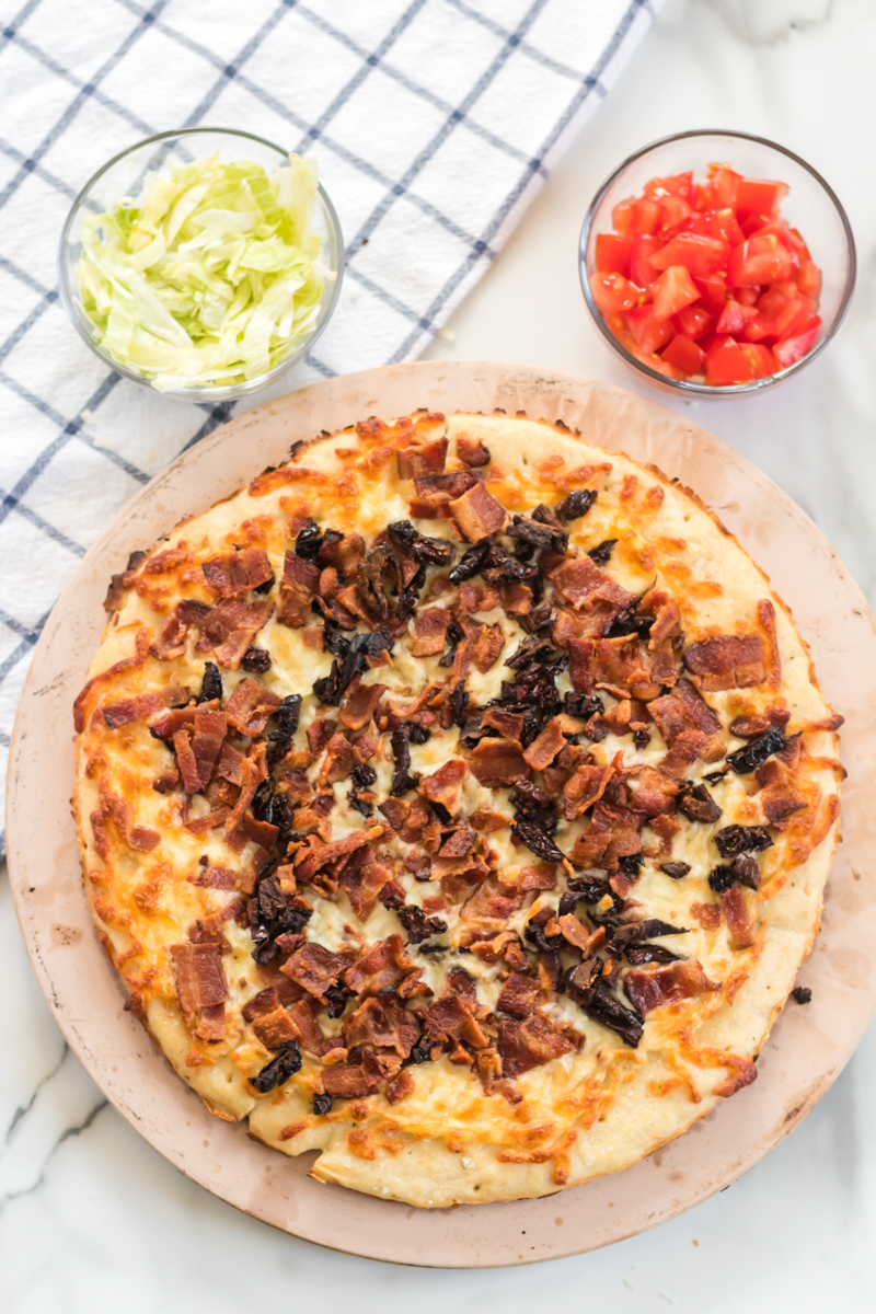 This BLT Pizza is semi-homemade and topped with cheese, bacon, lettuce, and tomatoes then drizzled with ranch dressing - a super easy meal for pizza night at home! | www.persnicketyplates.com pizza with melted cheese ready to top with lettuce & tomatoes for blt pizza