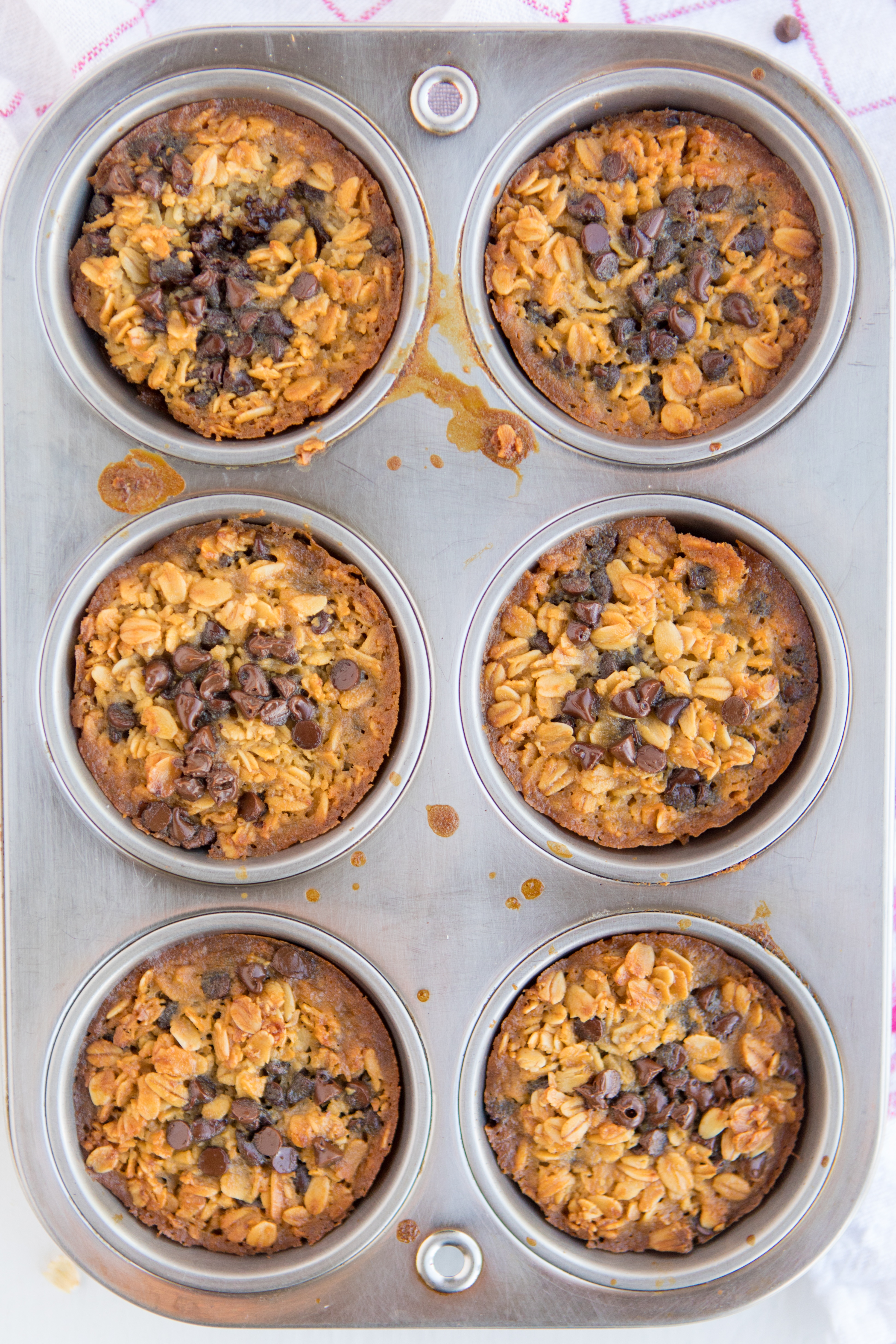 Baked Oatmeal Chocolate Chip Breakfast Cups are the perfect option for on-the-go breakfast! Swap out the chocolate chips for fruit, nuts, or spices for variety. | www.persnicketyplates.com muffin pan of 6 Baked Oatmeal Breakfast Cups sprinkled with mini chocolate chips fresh from the oven