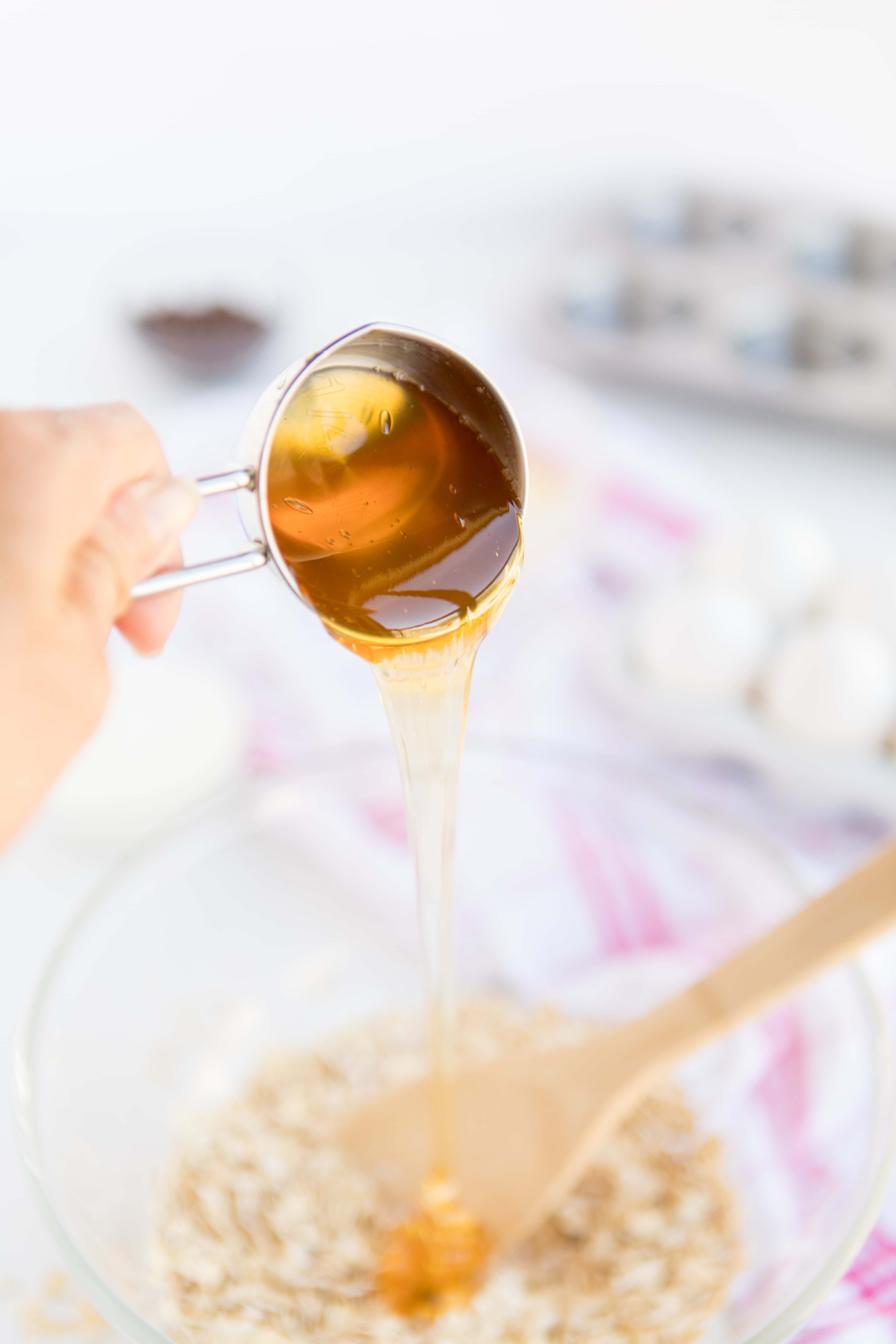 Baked Oatmeal Chocolate Chip Breakfast Cups are the perfect option for on-the-go breakfast! Swap out the chocolate chips for fruit, nuts, or spices for variety. | www.persnicketyplates.com pouring honey from a measuring cup inot a bowl to make Baked Oatmeal Breakfast Cups