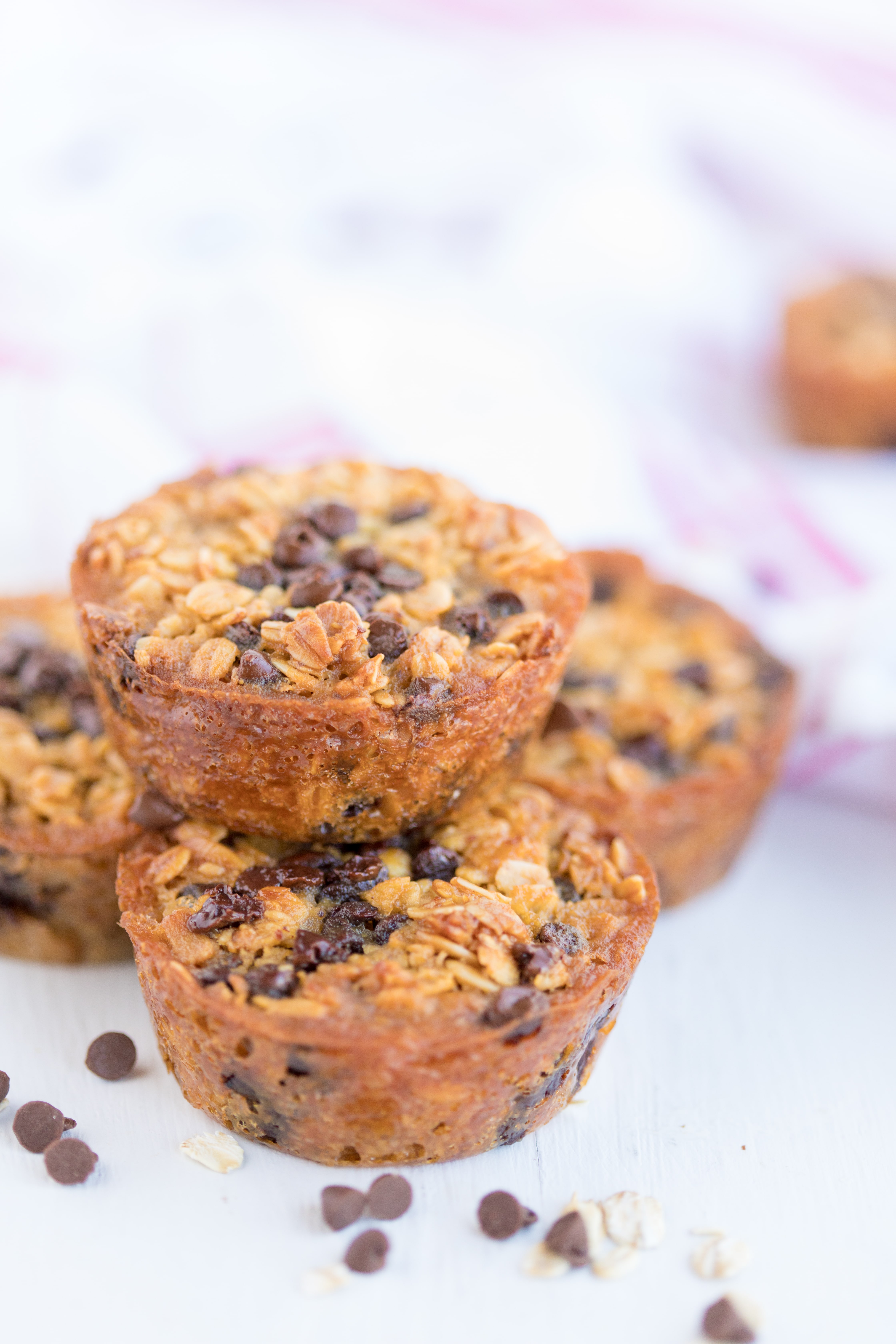 Baked Oatmeal Chocolate Chip Breakfast Cups are the perfect option for on-the-go breakfast! Swap out the chocolate chips for fruit, nuts, or spices for variety. | www.persnicketyplates.com stack of 4 baked oatmeal chocolate chip breakfast cups with scattered chocolate chips