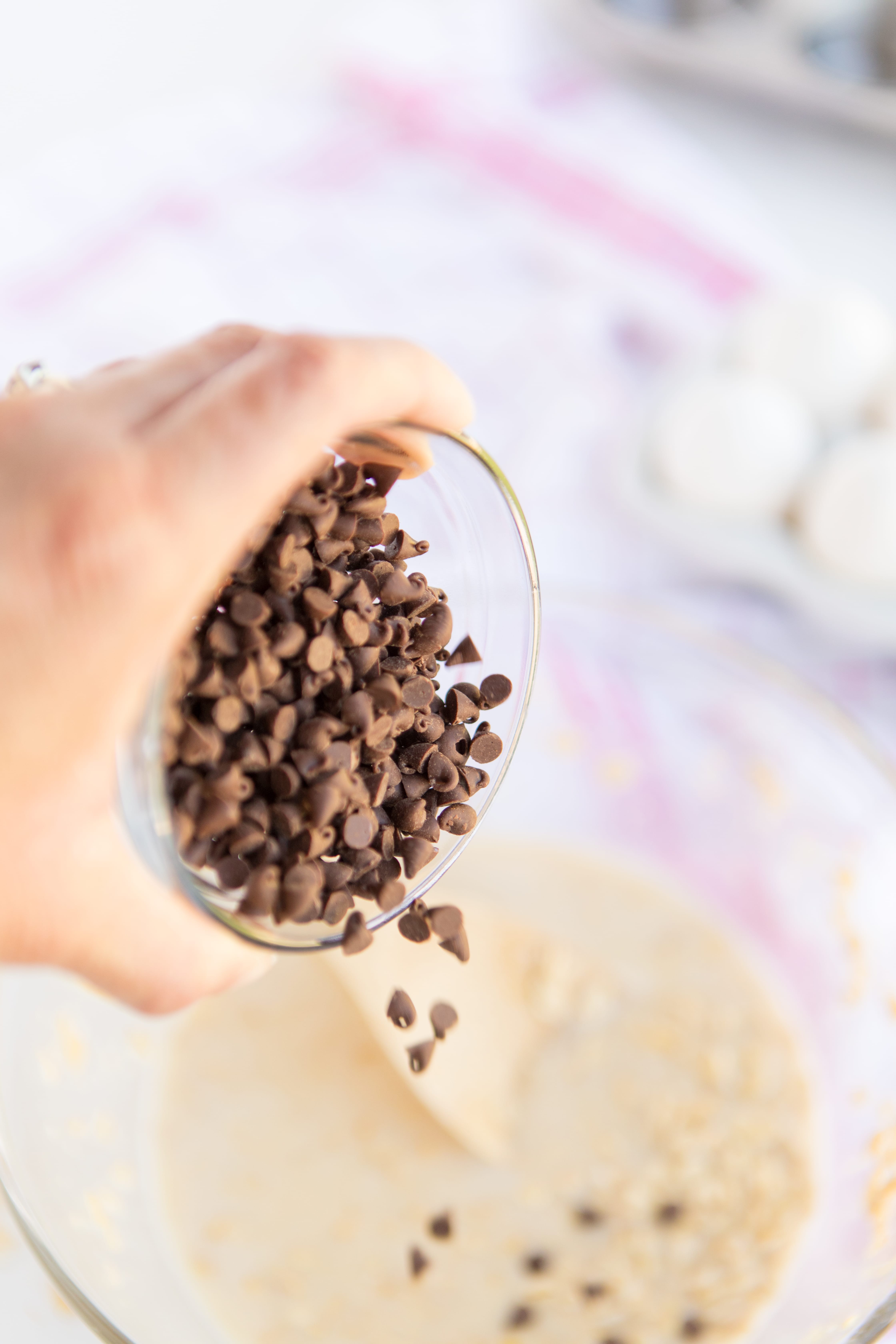 Baked Oatmeal Chocolate Chip Breakfast Cups are the perfect option for on-the-go breakfast! Swap out the chocolate chips for fruit, nuts, or spices for variety. | www.persnicketyplates.com pouring mini chocolate chips into Baked Oatmeal Breakfast Cups batter