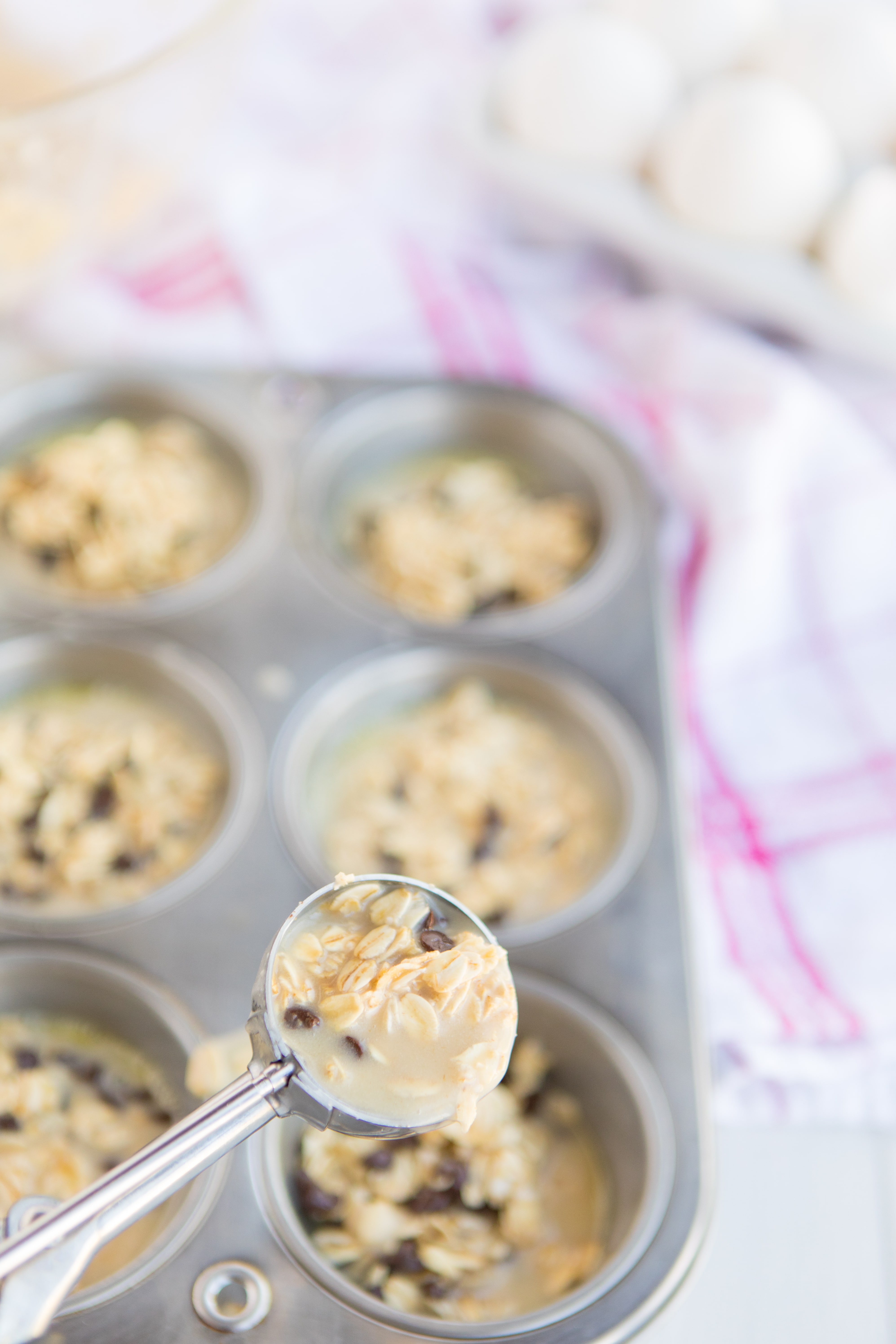 Baked Oatmeal Chocolate Chip Breakfast Cups are the perfect option for on-the-go breakfast! Swap out the chocolate chips for fruit, nuts, or spices for variety. | www.persnicketyplates.com muffin pan of Baked Oatmeal Breakfast Cups with a cookie scoop portioning out batter