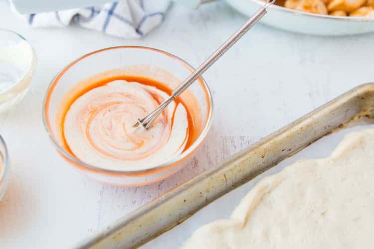 Buffalo Chicken Bread is easy to make at home & better than take-out! Stuffed bread recipes make the perfect weeknight dinner, and they're great for serving at parties or as game day snack food. This easy stuffed bread recipe starts with pizza dough then is filled with spicy Buffalo chicken and cheese. SO delicious! | www.persnicketyplates.com buffalo sauce mixed with ranch in small bowl