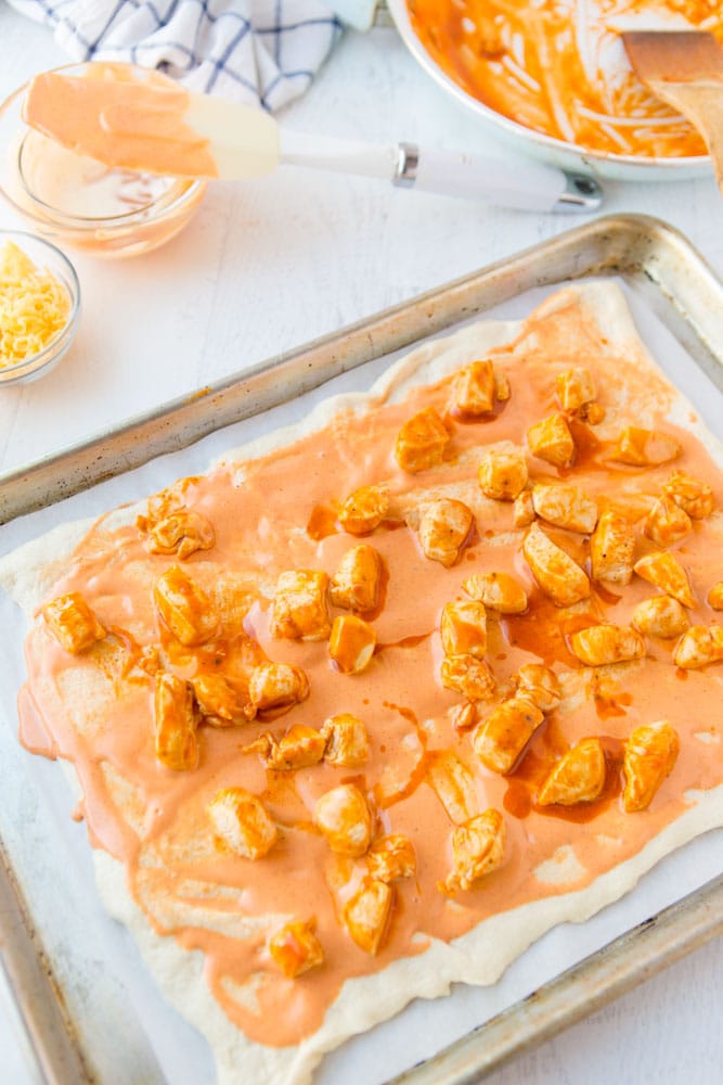 Buffalo Chicken Bread is easy to make at home & better than take-out! Stuffed bread recipes make the perfect weeknight dinner, and they're great for serving at parties or as game day snack food. This easy stuffed bread recipe starts with pizza dough then is filled with spicy Buffalo chicken and cheese. SO delicious! | www.persnicketyplates.com pizza crust topped with buffalo sauce and cooked chicken