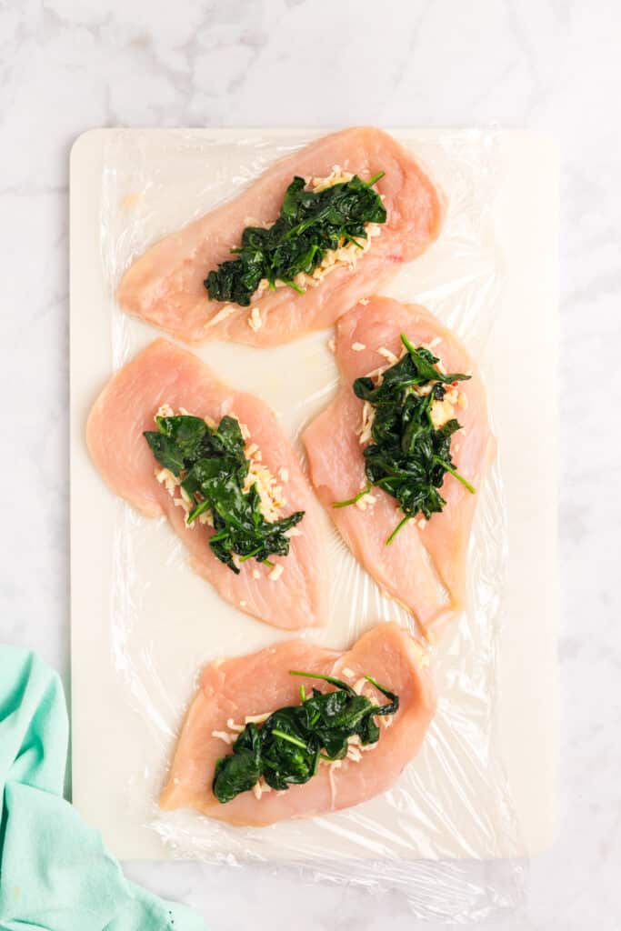 Raw chicken breasts being stuffed with cheese and spinach.