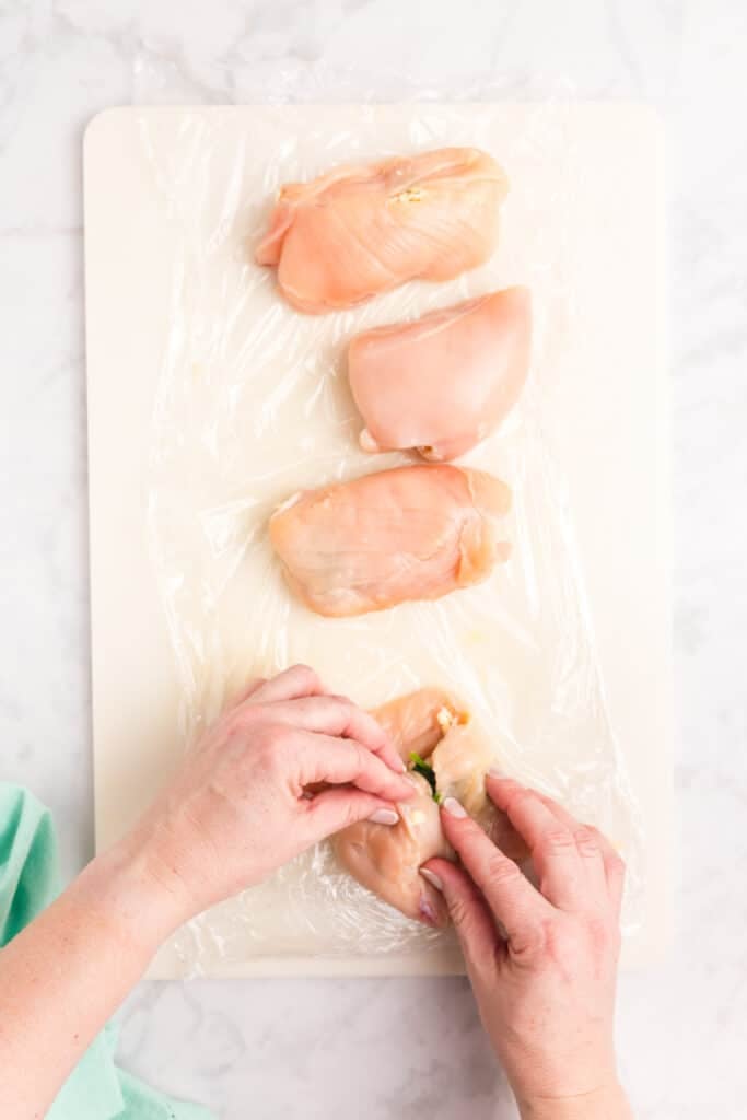A step-by-step process of preparing Cajun stuffed chicken breasts, showing hands stuffing raw chicken breasts with cheese and spinach on a white cutting board.