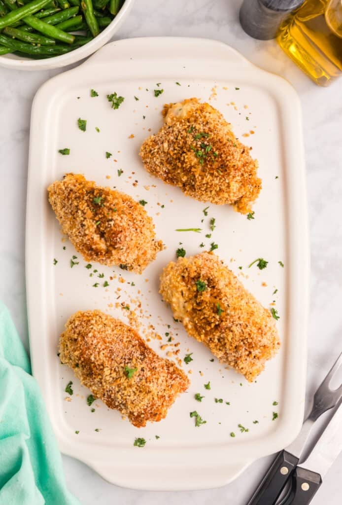 Crispy Cajun stuffed chicken breasts garnished with herbs on a white platter.