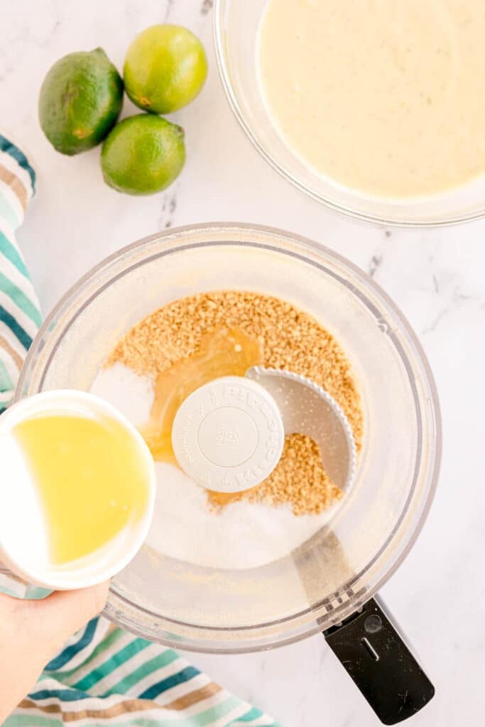 melted butter being poured into a food processor with graham cracker crumbs.