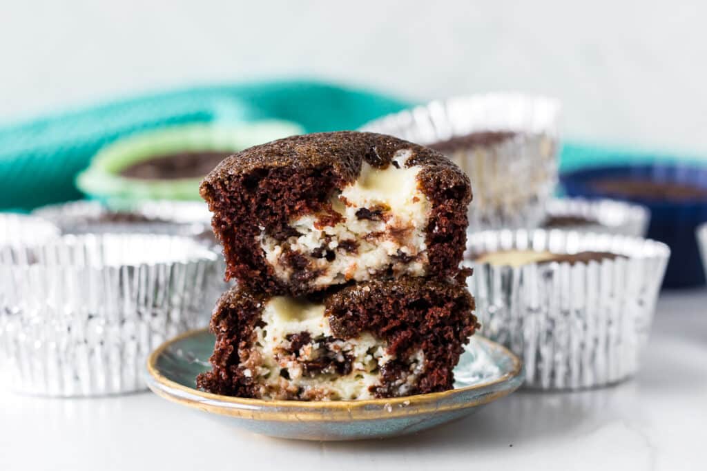 A close-up of a chocolate cupcake with a creamy cheesecake center and chocolate chips, broken in half.