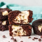A close-up of a chocolate cupcake with a creamy cheesecake center and chocolate chips, broken in half and stacked on top of each other.