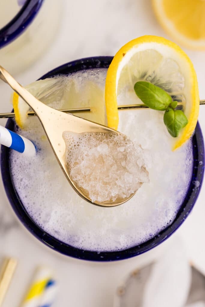 A gold spoon scooping up crushed frozen lemonade from a glass.