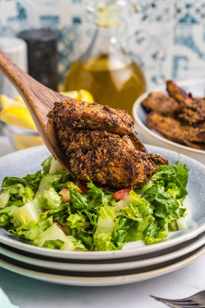 spoon topping zaatar chicken onto a salad.