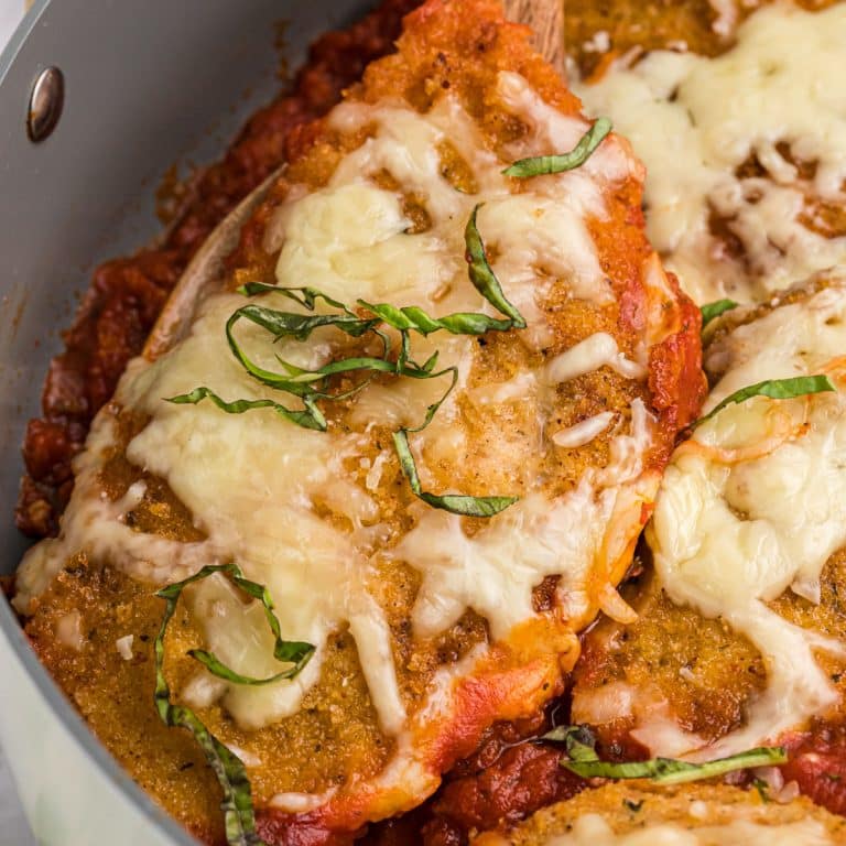 spoon lifting a chicken breast with mozzarella from a skillet.