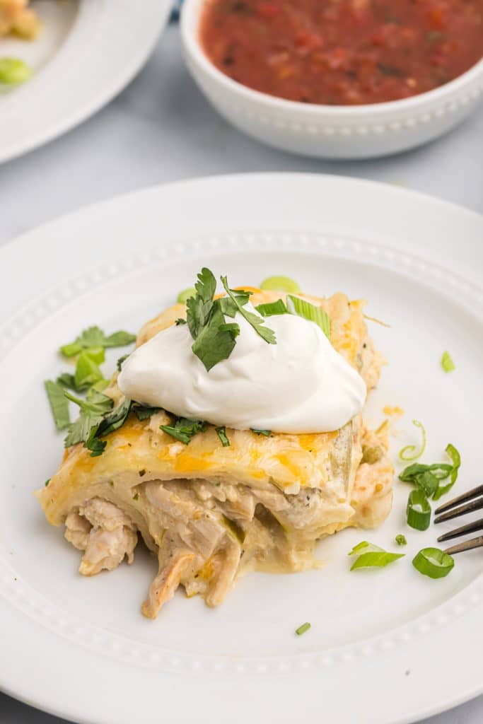 a verde chicken enchilada on a white plate topped with cilantro & sour cream.