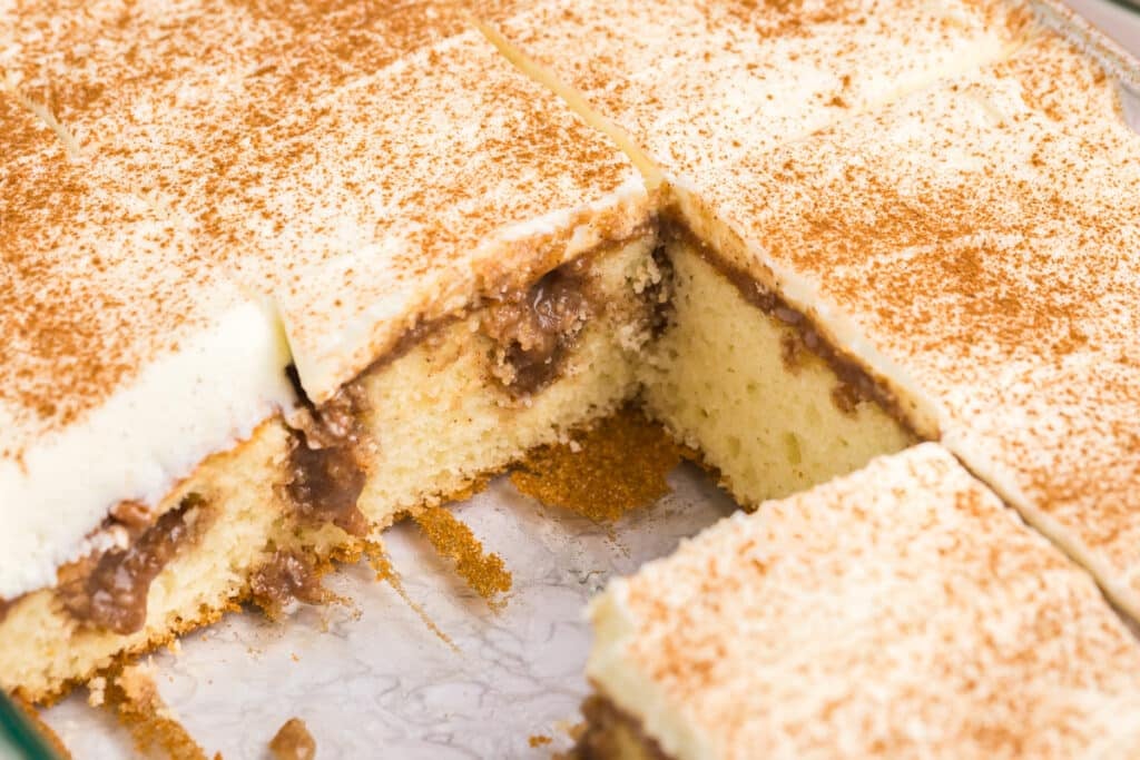 side view of a sliced cinnamon roll poke cake with cream cheese frosting.