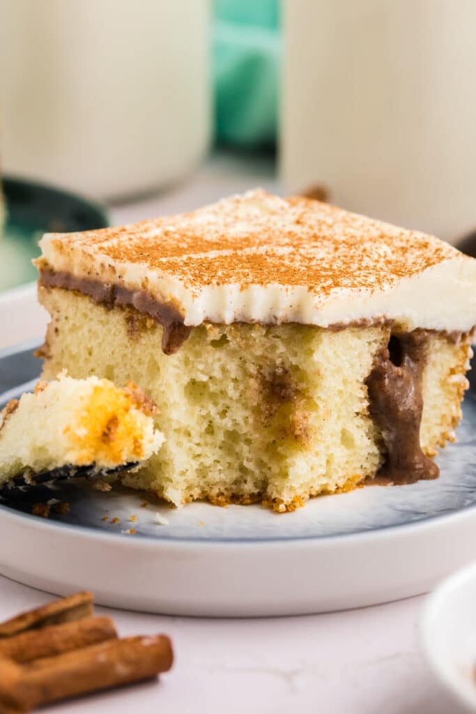 a bite missing from a slice of cinnamon roll poke cake with cream cheese frosting.