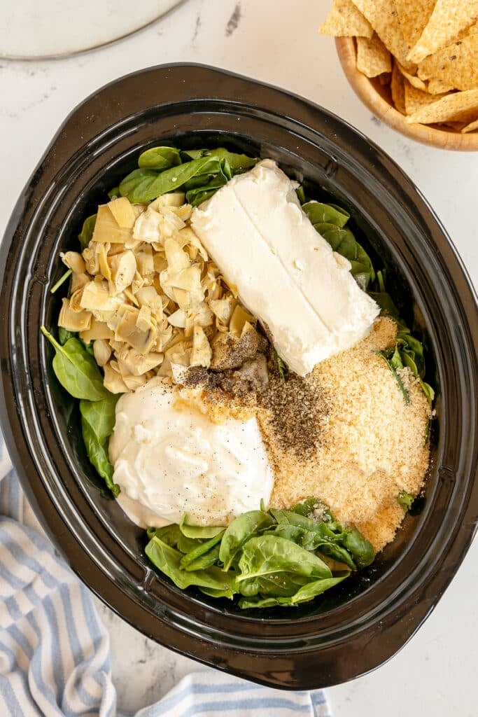 overhead shot of ingredients in a crockpot to make spinach artichoke dip.