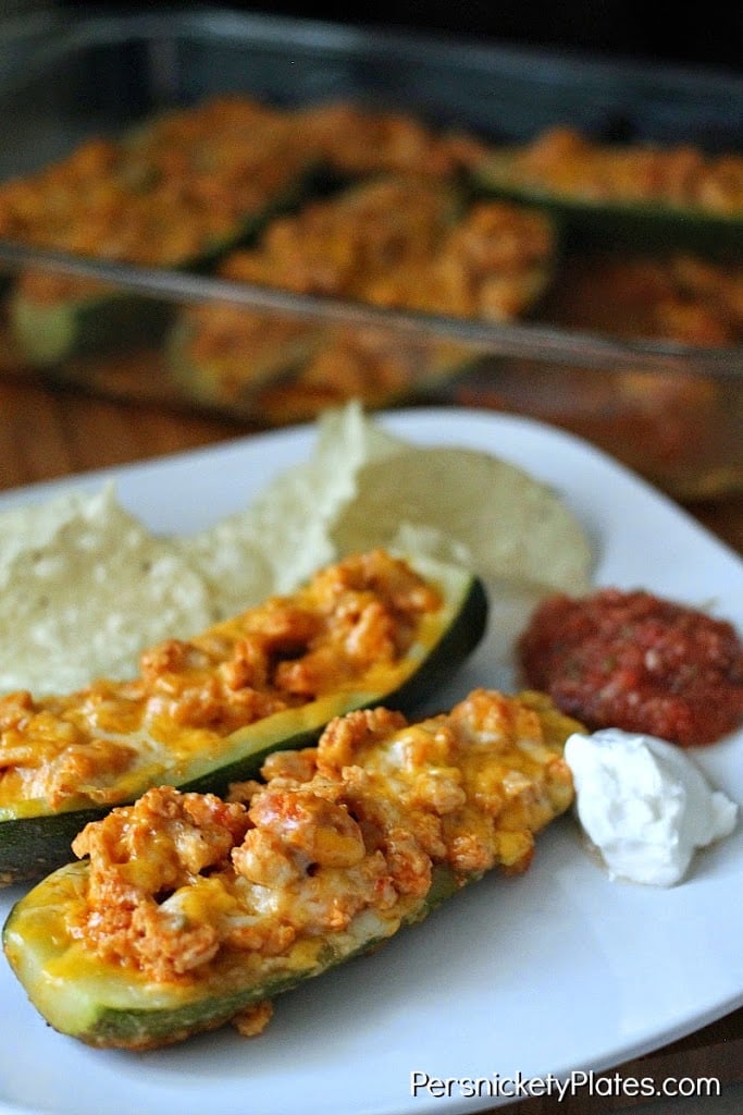 two zucchini taco boats on white plate with salsa & sour cream