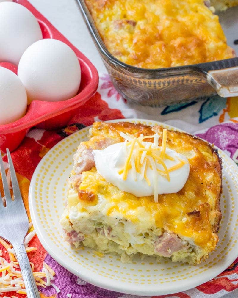 serving of ham & potato breakfast casserole on a plate next to fresh eggs