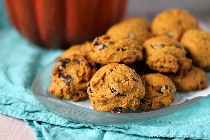clear plate of pumpkin chocolate chip cookies on a teal napkin with a pumpkin in the background