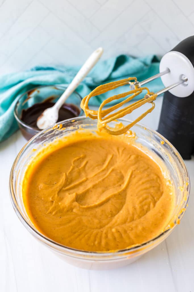 pumpkin cake batter in a mixing bowl with a hand mixer.