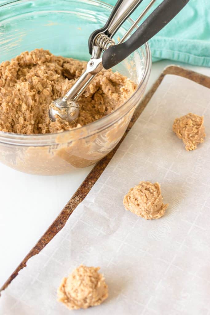 mixing bowl of oatmeal cookie dough scooping dough onto a baking sheet.