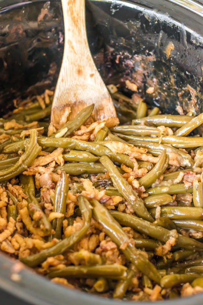 wooden spoon sticking into a crockpot of green bean casserole.