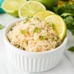 white bowl filled with rice topped with cilantro and lime wedges.