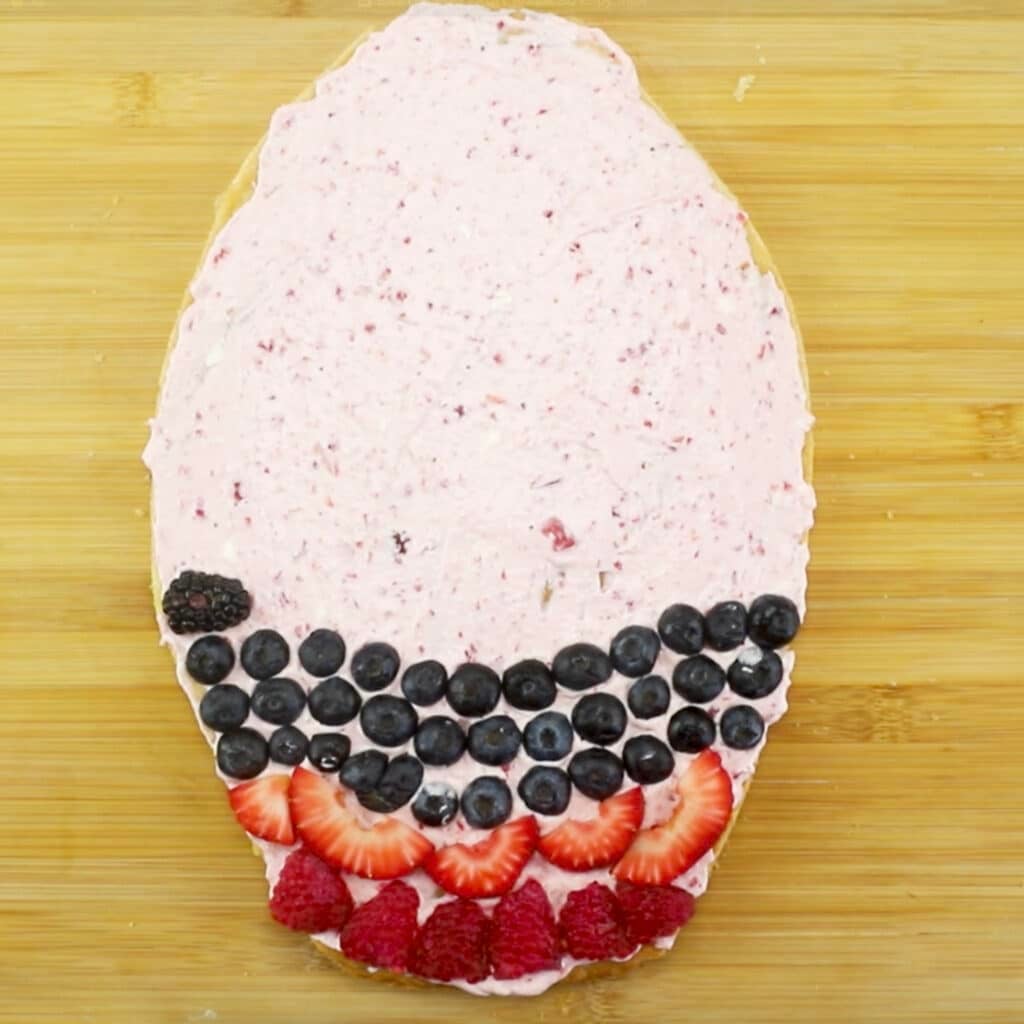 partially decorated easter egg fruit pizza with cream cheese frosting.