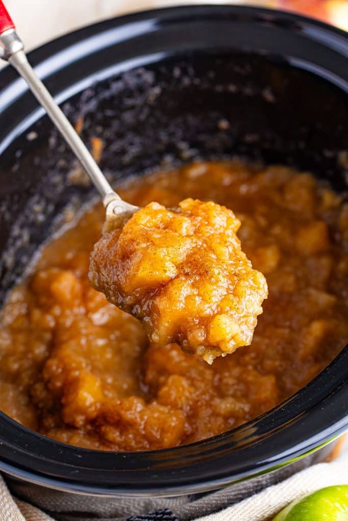 spoon lifting a scoop of applesauce from a slow cooker.