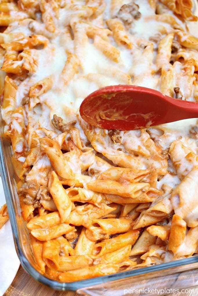baked mostaccioli with a portion taken out and a red serving spoon 