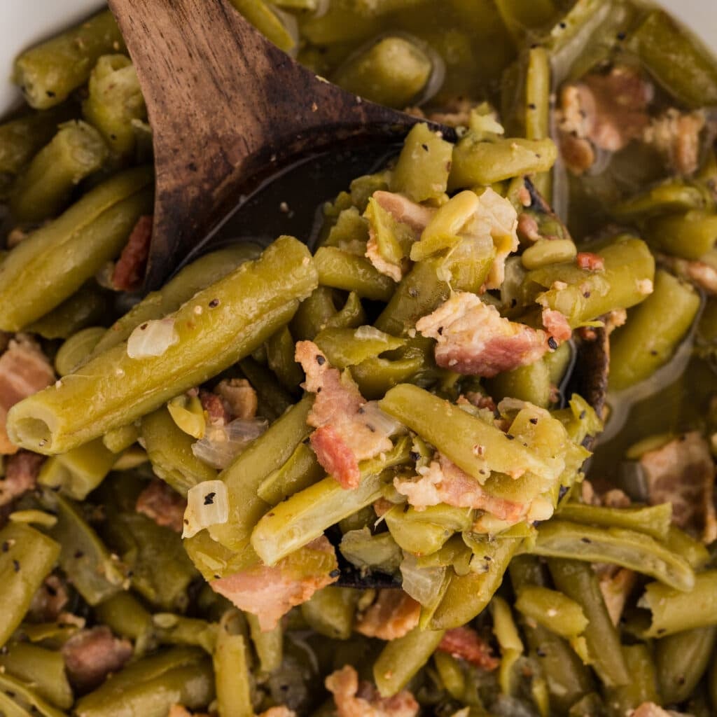 Green beans with bacon and onion on a wooden spoon over a pot.