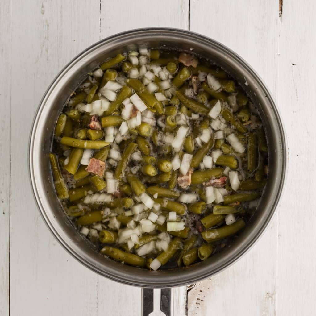 overhead shot of green beans, onion, and bacon in a saucepan.