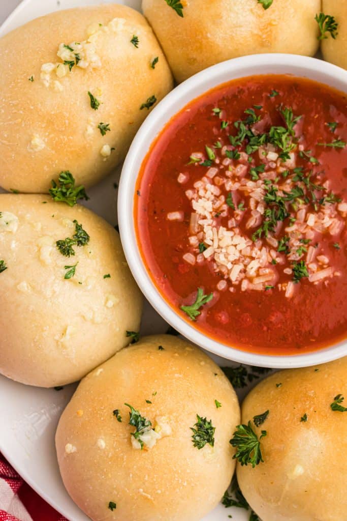 overhead shot of rolls topped with parsley & garlic next to a bowl of marinara dipping sauce.