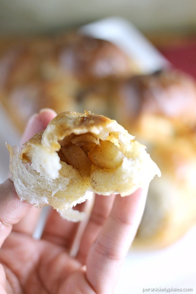 Apple Filled Pull Apart Bread is sticky and sweet and easy to make with the help of Rhodes Dinner Rolls! Pick your favorite fall apples and let your kids help you put together this simple dessert. | Persnickety Plates close up of apple filled pull apart bread in a hand