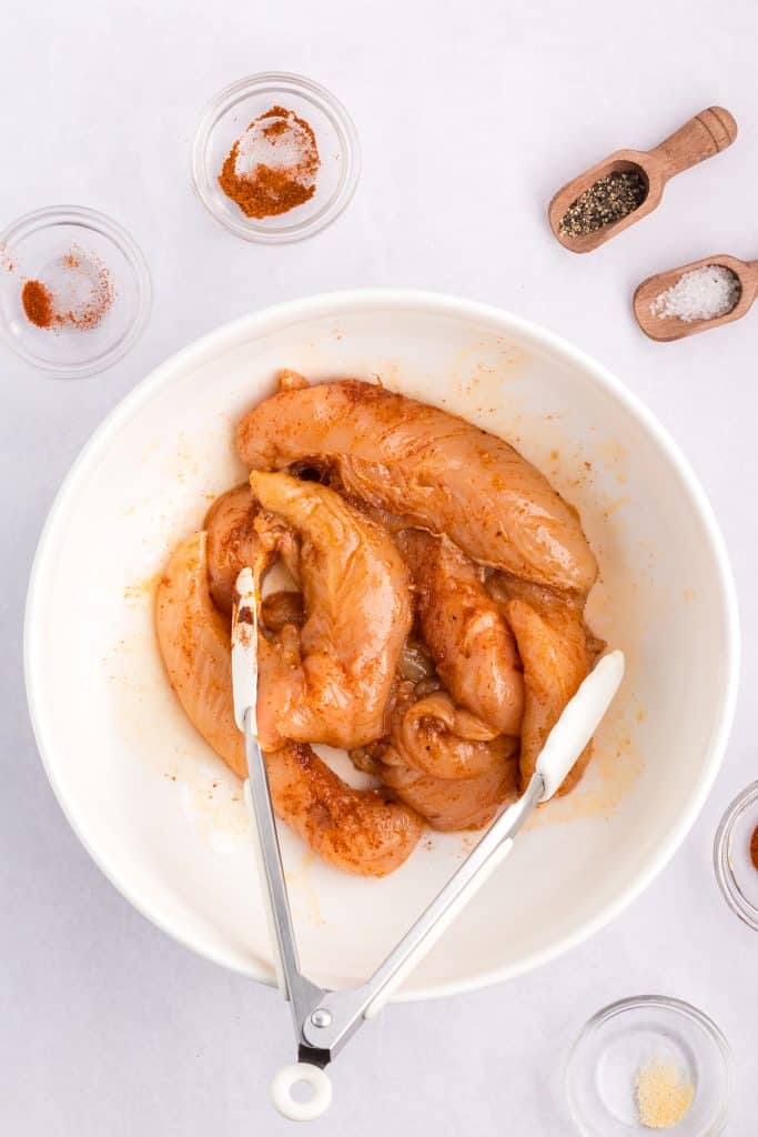 tongs with raw chicken in a bowl.